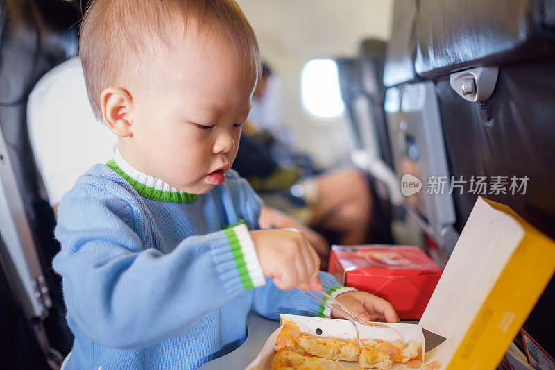 可爱的18个月/ 1岁的亚洲小男孩穿着蓝色毛衣在飞机上吃东西